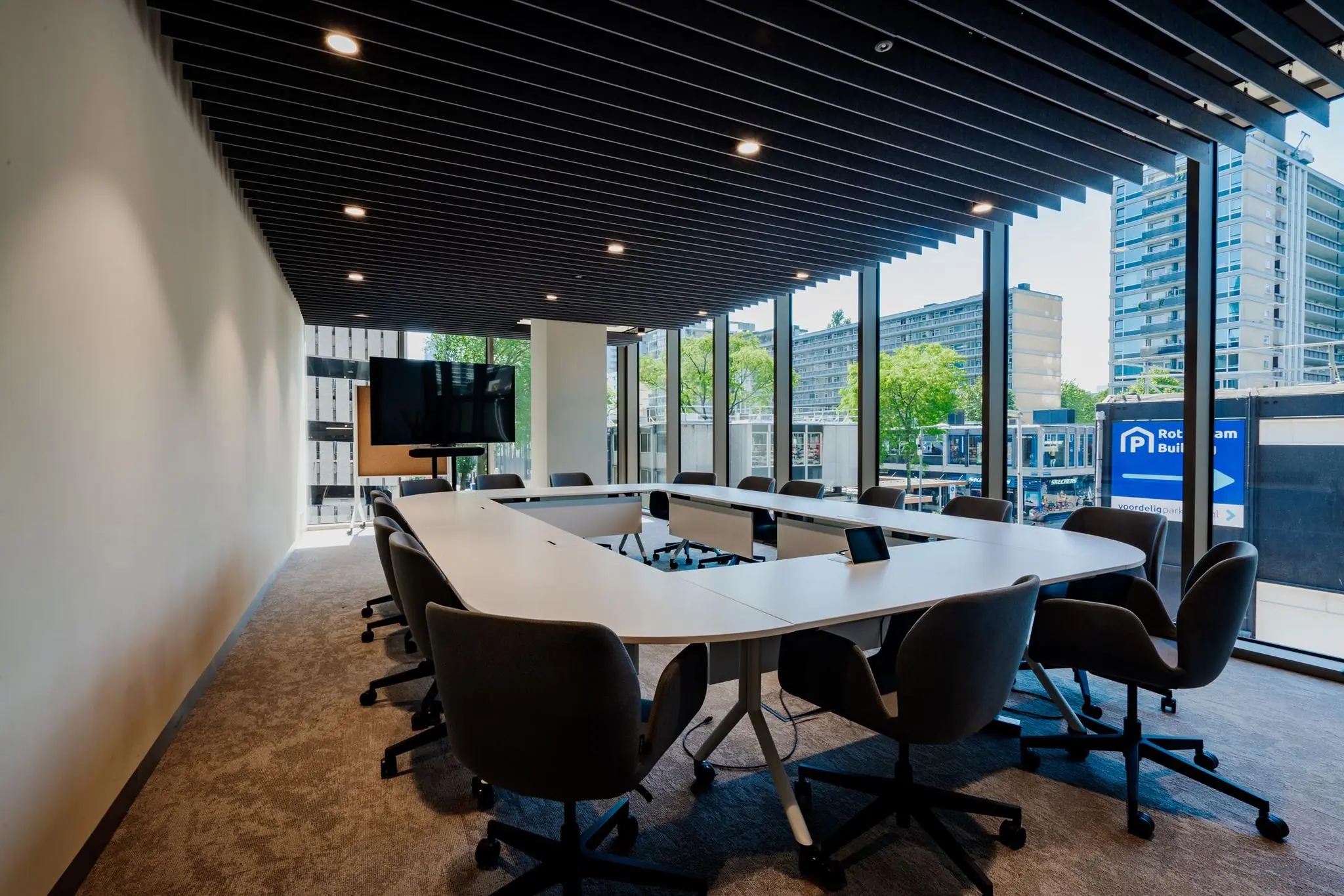 Vergaderruimte met U-vormige tafel, moderne bureaustoelen en uitzicht op de Aert van Nesstraat in Rotterdam.